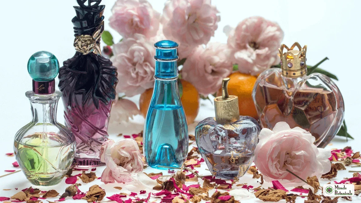 Assorted decorative glass perfume bottles among pink roses, oranges and scattered dried rose petals