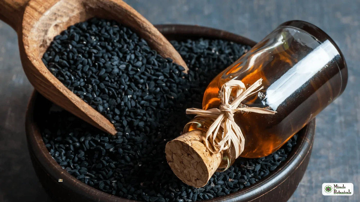 Corked bottle of golden oil resting in a wooden bowl of black seeds beside a wooden scoop