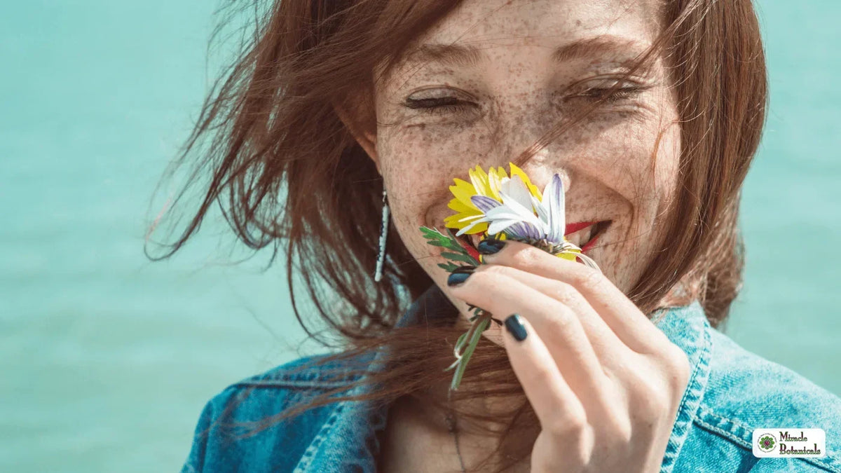Smiling freckled woman with windblown red hair smelling a small bunch of yellow and white flowers