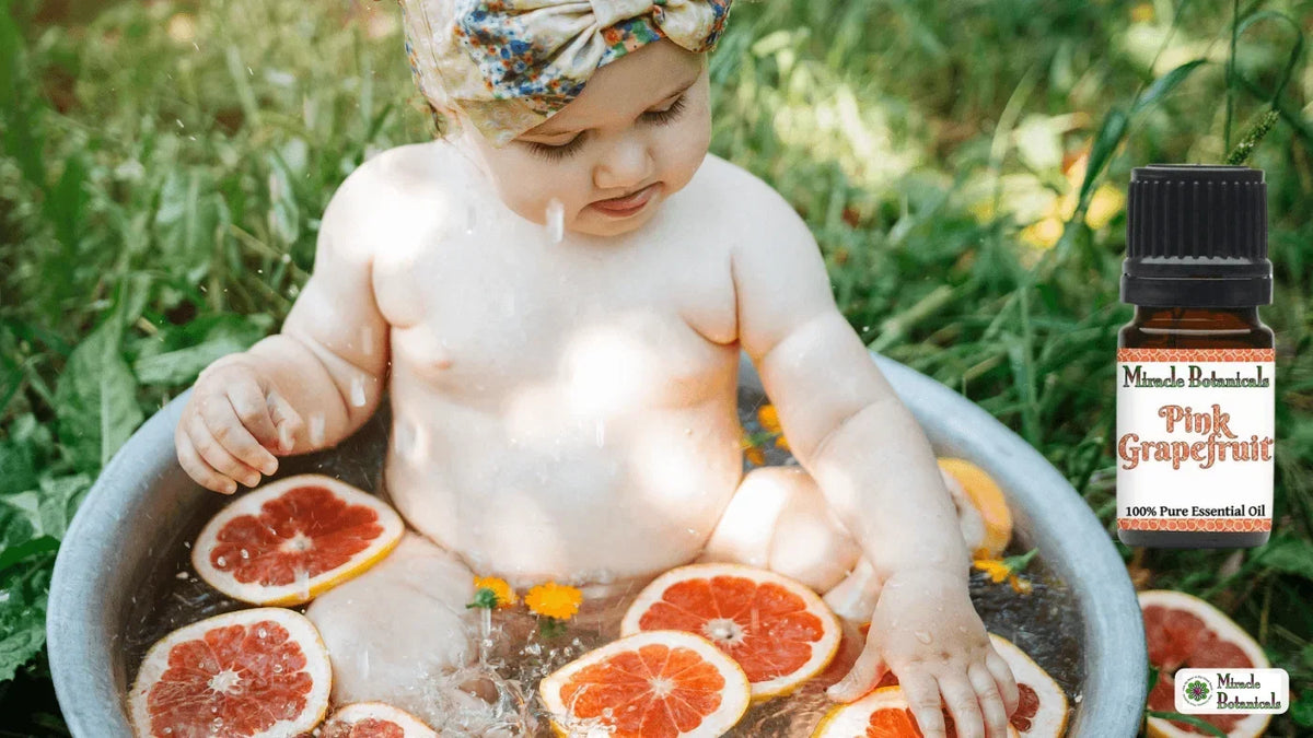 Baby bathing in an outdoor tub with grapefruit slices beside a Miracle Botanicals Pink Grapefruit essential oil bottle
