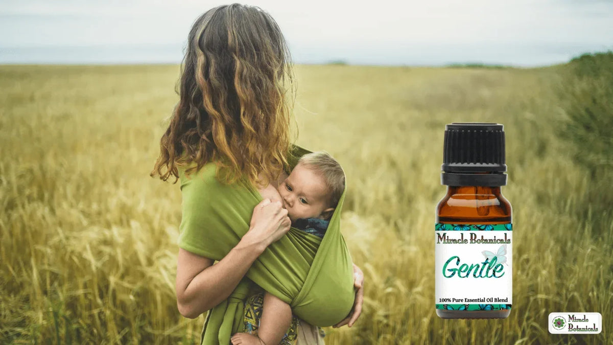 Woman breastfeeding a baby in a green sling in a grain field beside a Gentle essential oil blend bottle
