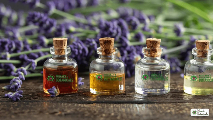 Four corked glass bottles of oils from amber to clear, labeled Miracle Botanicals, with lavender sprigs on wood